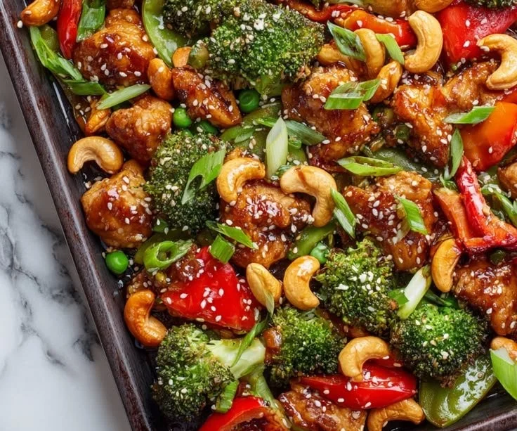 Sheet pan chicken with cashews and mixed vegetables on a baking tray