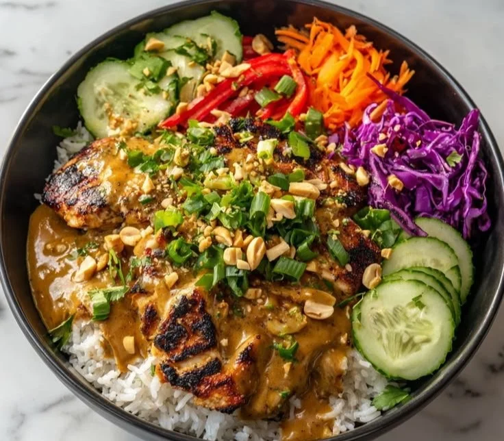 Thai-inspired peanut chicken bowl with fresh vegetables and peanut sauce