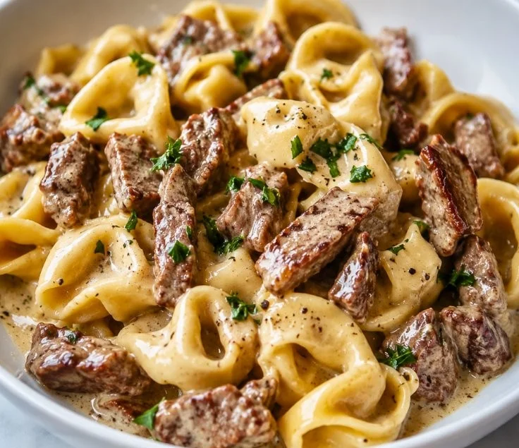 Bowl of creamy Philly Cheesesteak Tortellini topped with cheese and herbs.